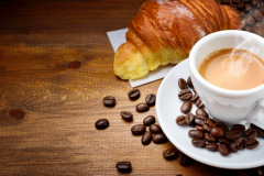 Espresso and croissant with coffee beans on wood background